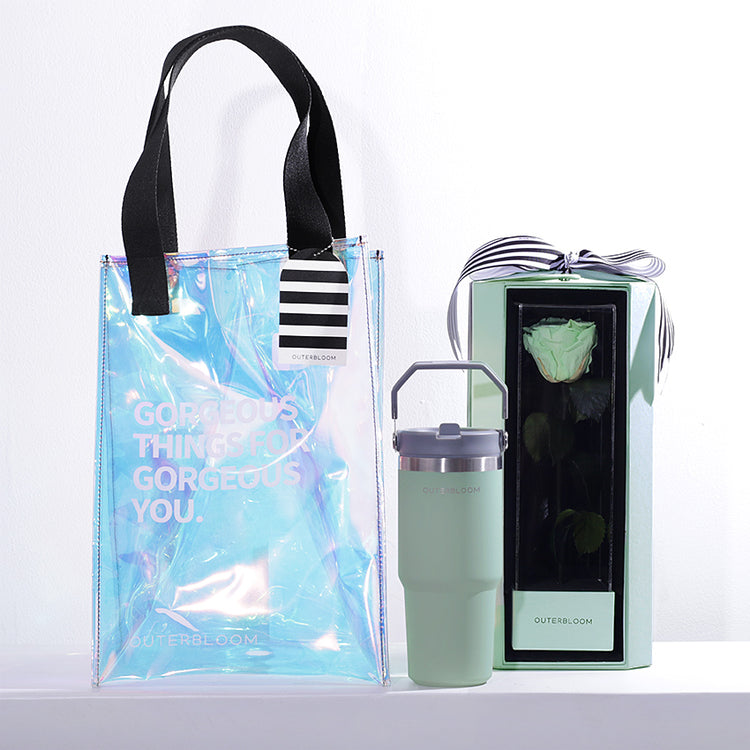 A chic and modern gift set with a mint and iridescent theme. The hamper includes a large, transparent holographic tote bag with black handles and the text "GORGEOUS THINGS FOR GORGEOUS YOU." The bag also features a black-and-white striped tag. The set contains a tall, mint green tumbler with a grey handle. The set also includes a matching green box that showcases a single, beautifully preserved mint green rose. This stylish and thoughtful hamper is a perfect gift for someone special.
