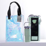 A chic and modern gift set with a mint and iridescent theme. The hamper includes a large, transparent holographic tote bag with black handles and the text "GORGEOUS THINGS FOR GORGEOUS YOU." The bag also features a black-and-white striped tag. The set contains a tall, mint green tumbler with a grey handle. The set also includes a matching green box that showcases a single, beautifully preserved mint green rose. This stylish and thoughtful hamper is a perfect gift for someone special.