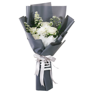 An elegant bouquet featuring a monochromatic white and grey theme. The arrangement is composed of classic white roses, asters, and peacock, delicate baby's breath, and other smaller white filler flowers. The flowers are wrapped in a clean, white inner layer and a sophisticated grey outer layer. The bouquet is tied with a double white ribbon—and a small tag. The minimalist style makes it a thoughtful gift for any occasion.